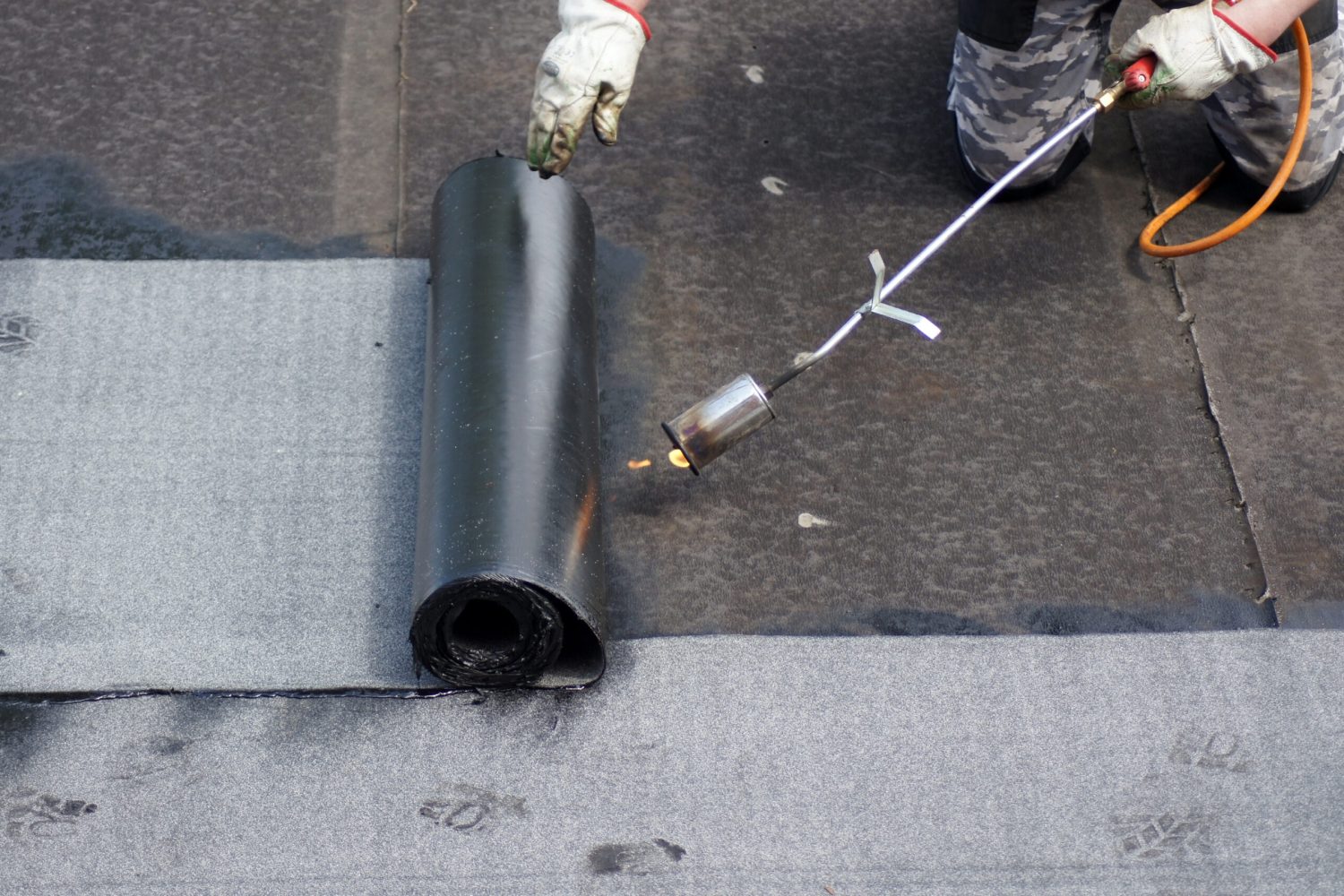 The flat roof installation with propane blowtorch during construction works with roofing felt